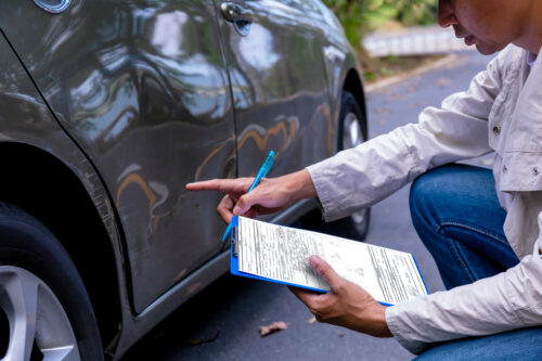 insurance adjuster person examining a car with a clipboard and pen in hand